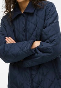 Mornarsko prešitje jakno z žametnim ovratnikom, diamanti, gumbi na pritiskanje in rebrastimi manšeti, z gladko, sijočo teksturo.