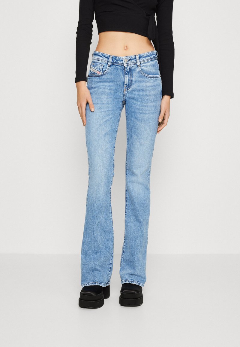 Hellblaue, ausgestellte Jeans aus Denim mit einem Knopf- und Reißverschluss, ausgestattet mit Fronttaschen und einem leichten Wasch-Effekt, kombiniert mit schwarzen Plateauschuhen.
