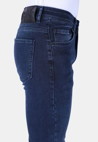 Donkerblauwe denim jeans met een slim fit, met een achterzak, stikdetails en een leren taillebandlabel. Glad textuur, klassiek ontwerp.