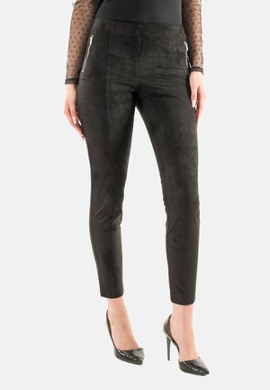 Pantaloni in finta suede nera con vestibilità slim, dotati di tasche con zip frontali e una texture liscia e opaca. Abbinati a tacchi alti neri.