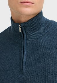 Granatowy sweter dzianinowy z wysokim kołnierzem i pół zamkiem. Posiada strukturalny wzór oraz srebrną suwakiem z logo.