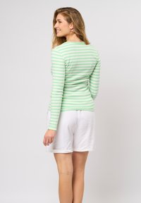 Langarmshirt in lichtgroen met witte horizontale strepen, gedragen met witte shorts. De stof ziet er glad uit met een aansluitend ontwerp.