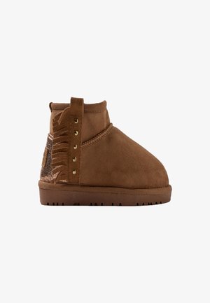 Bottines en suède marron avec un bout arrondi, présentant un détail à franges et des accents métalliques à l'arrière. Semelle en caoutchouc avec un motif de traction.