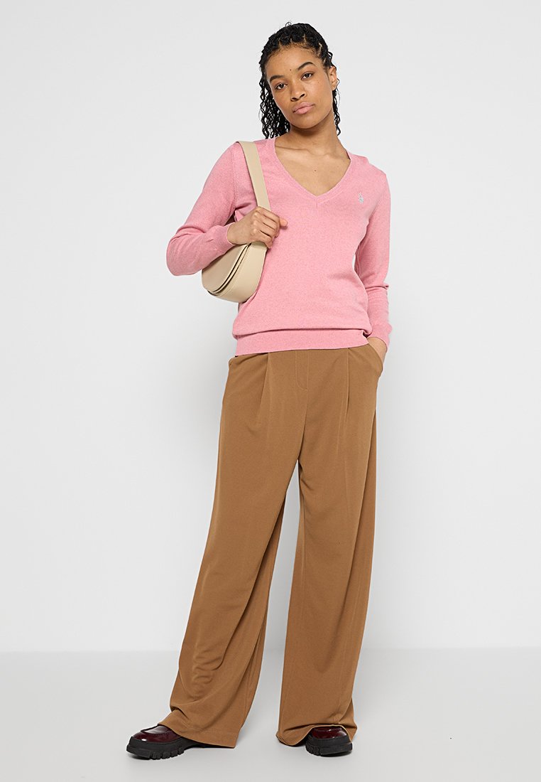 Maglione rosa a scollo a V e pantaloni larghi marroni. Il maglione è realizzato in materiale morbido, mentre i pantaloni presentano dettagli plissettati e una texture liscia.