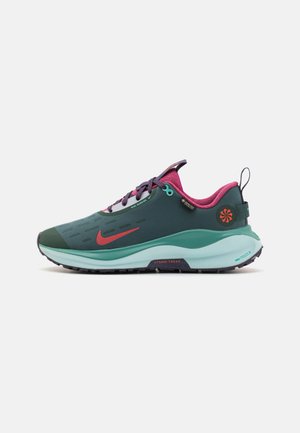 Nike skriešanas apavi ar tumši zaļu virsu, purpura akcentiem un zila zoli. Iezīmējas ar vieglu dizainu un teksturētām virsmām, kas nodrošina saķeri.