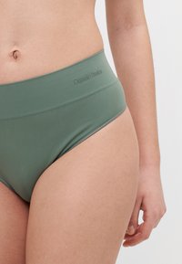 High-waisted green bikini bottom made of smooth, stretchy fabric. Features subtle branding and a wide waistband for comfort.