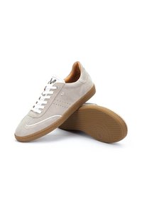 Zapatillas de ante gris claro con acentos blancos, puntera redonda, suela de goma texturizada en color marrón, y detalles perforados en los laterales. Cierre con cordones.
