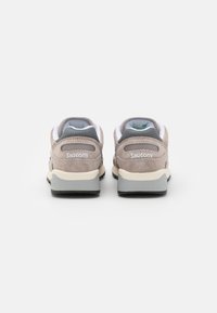 Vista posteriore di sneakers in suede grigio con accenti bianchi, intersuola beige e suola in gomma nera. Presenta un logo in rilievo sul tallone.