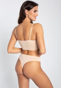 Braletka i stringi w kolorze nude wykonane z miękkiego, elastycznego materiału; mają cienkie ramiączka oraz bezszwowy design zapewniający gładki wygląd.
