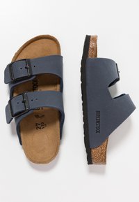 Blå tvåremmade sandaler med justerbara spännen, korkfotbädd och texturerad gummiyttersula. Varumärket "Birkenstock" synligt på sidan.