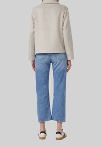 Beige wollen-blend jas met een korte snit, gecombineerd met mid-blue wijde jeans. Kenmerkt zwarte sneakers met een crèmekleurige zool.