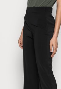 Svart skräddarsydda byxor med en mjuk textur, hög midja och sidfickor, med en slim fit och veckdetaljer längs benen.