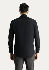 Camicia nera a maniche lunghe con orlo curvo, texture liscia e polsini con bottoni, vista dal retro. Nessun motivo o logo visibile.