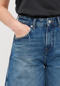 Jeans aus Denim in mittlerem Blau mit hoher Taille, vorderen Taschen und Reißverschluss. Mit klassischer Naht und metallischen Hardware-Details.