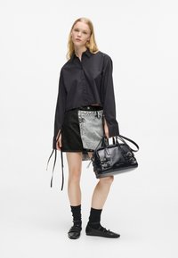 Μαύρο κοντομάνικο πουκάμισο με κουμπιά, τζιν φούστα με ανοιχτούς και σκούρους πάνελ, μαύρη τσάντα με αγκροβίδες, μαύρες κάλτσες και φλατ παπούτσια.