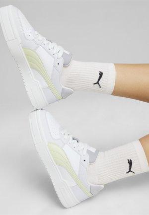 Baskets blanches avec des accents gris et vert clair, en cuir texturé et matériaux en maille, semelles plates, accompagnées de chaussettes blanches à côtes avec un logo.