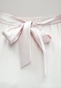 Világos rózsaszín selyemszalag masnira kötve egy texturált fehér anyag körül, amely függőleges bordázott részleteket és bővülő szoknyasziluettet mutat.