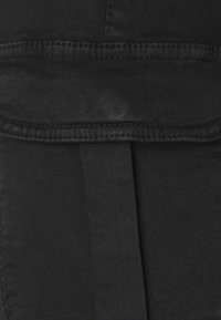 Černá denimo tkanina s hladkou strukturou, s výrazným švem a detailním složeným lemem. Jednoduchý a minimalistický design.