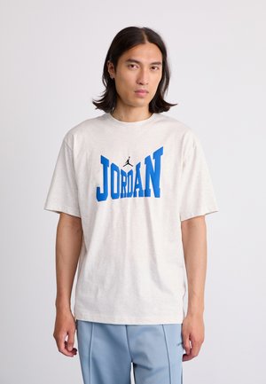 Šviesiai pilka medvilninė marškinėliai su dideliu mėlynu užrašu "JORDAN" ir mažuoju juodu logotipu. Atsipalaidavęs siluetas, trumpomis rankovėmis ir apvaliu iškirpimu.