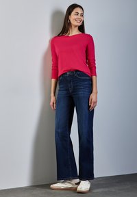 Dopasowana, jasnoróżowa bluzka z długim rękawem, zestawiona z ciemnoniebieskimi dżinsami dzwonami i białymi sneakersami. Prosty design z minimalnym zdobieniem.