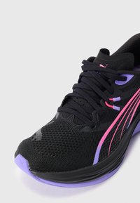 Chaussure de course noire avec des accents violets et roses, dessus en mesh et lacets noirs sur un fond clair.