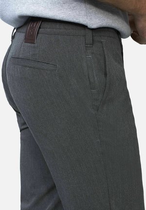 Man die donkergrijze formele broek draagt met zij- en achterzakken, gecombineerd met een lichtgrijs overhemd dat in de broek is gestopt.