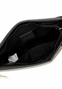 Interno di una borsa a tracolla in pelle nera, con una tasca con zip, foderato in tessuto liscio e un piccolo cartellino. L'esterno ha una finitura testurizzata.