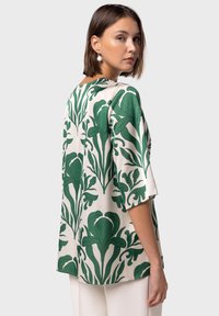 Blusa verde a fantasia floreale con maniche corte, realizzata in tessuto morbido. Presenta uno sfondo crema e un design dal fit rilassato.