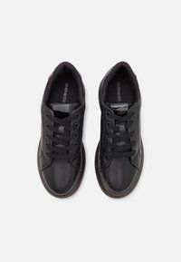 Černé tenisky s hladkým koženým svrškem, kulatou špičkou a strukturovanou gumovou podrážkou. Obsahují černé tkaničky a minimalistické designové akcenty.