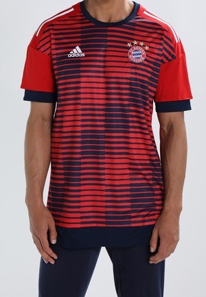 Homme portant un maillot de football FC Bayern Munich rayé rouge et marine avec logo Adidas, manches courtes et bordure marine au col et aux manches.