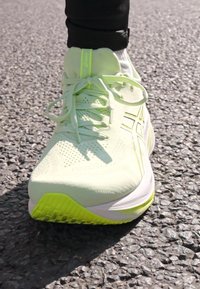 Scarpa da running verde chiaro con una tomaia in rete traspirante, superficie testurizzata e accenti gialli brillanti sulla suola e sulla linguetta.