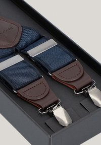 Granatowe elastyczne szelki z skórzanymi akcentami, srebrnymi metalowymi klipsami i wzmocnionymi szwami, zaprezentowane w czarnym pudełku.
