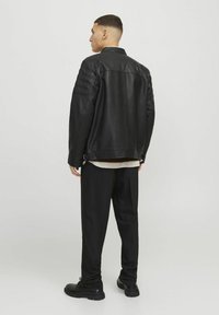 Svart läderjacka med texturerade axelpaneler, öppen krage och lös passform, i kombination med svarta byxor och svarta skor.