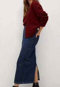 Burgundin väriin neulottu neuletakki, jossa on pitkät hihat ja napit, yhdistettynä tummansinisiin farkkuhameeseen, jossa on sivuhalkio ja taskut. Mustat nilkkurit.