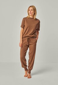 Brown loungewear set featuring a short-sleeve top with ribbed neckline and chest pocket, paired with tapered pants and adjustable waistband.