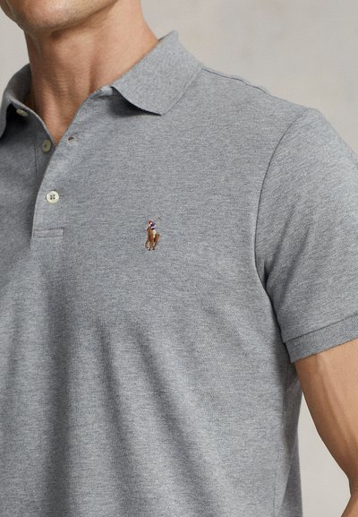 Muž nosi svetlosivé krátky rukáv polokošeľu s malým vyšívaným logom hráča póla na hrudi.