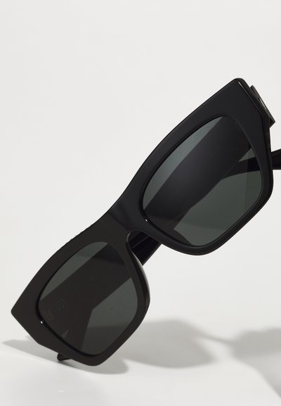 Occhiali da sole neri oversize con forma geometrica e lenti scure. Finitura lucida con montatura spessa e dettagli laterali discreti.