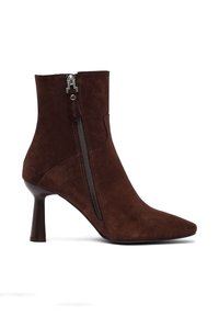 Stivale alla caviglia in suede marrone con punta appuntita, tacco affusolato e dettaglio con zip laterale. Texture liscia e design minimalista.