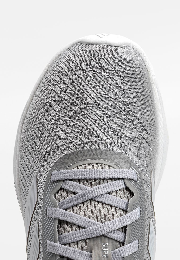 Grauer Sportschuh mit einem atmungsaktiven Mesh-Obermaterial, das auffällig mit strukturierten Mustern versehen ist, grauen Schnürsenkeln und einer weißen Gummisohle.