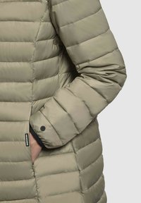 Vadderad jacka i ljus olivgrön. Har en quiltad design med en jämn textur, sidofickor och en tryckknappsdetalj på ärmen.
