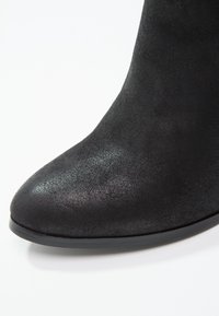 Bottine en daim noir avec bout arrondi et semelle plate sur fond blanc.