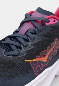Blue and black athletic shoe with mesh upper, pink accents, and contrasting logo. Features rounded toe and textured sole for grip.