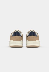 Καφέ σουέτ αθλητικά παπούτσια με λευκή σόλα, ναυτική ακμή στη φτέρνα και λείο επένδυση. Διαθέτουν στρογγυλή μύτη και υφή στην εξωτερική σόλα για καλύτερη πρόσφυση.