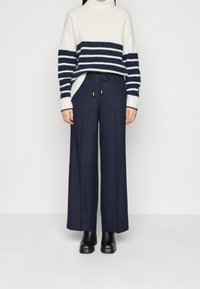 Vit och marinrandig tröja med polokrage, kombinerad med mörk marinblå vida byxor. Svarta ankelboots fulländar outfiten.