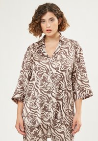 Bruin en crème gestreept knoopshirt met een losse pasvorm, brede mouwen en een voorkantzak. Glad stof met een zijdezachte textuur.