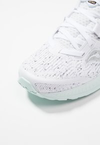 Bílé sportovní boty s texturovaným pleteným svrškem, s tečkovanými detaily, světle mátovými akcenty a flexibilní gumovou podrážkou. Obsahují ploché šňůrky a logo.