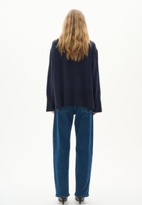 Marineblaues, übergroßes Sweatshirt mit langen Ärmeln, kombiniert mit hochgeschnittenen blauen Jeans. Glatte Textur, lockere Passform und minimale Details.
