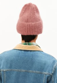 Roze gebreide muts met geribbelde textuur, zacht materiaal en een slouchy pasvorm. Draagt door een persoon in een spijkerjack over een geruite blouse.