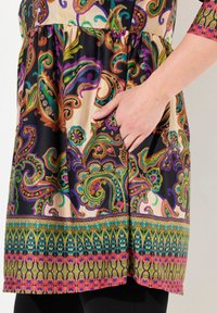 Multicolor tuniek met ingewikkeld paisley ontwerp in tinten paars, groen en oranje, met een zak aan de linkerkant en een decoratieve zoom.
