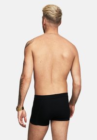 Svarta boxer kalsonger på en bar överkropp, med ett slätt, stretchigt material och en elastisk midja, sedd bakifrån.